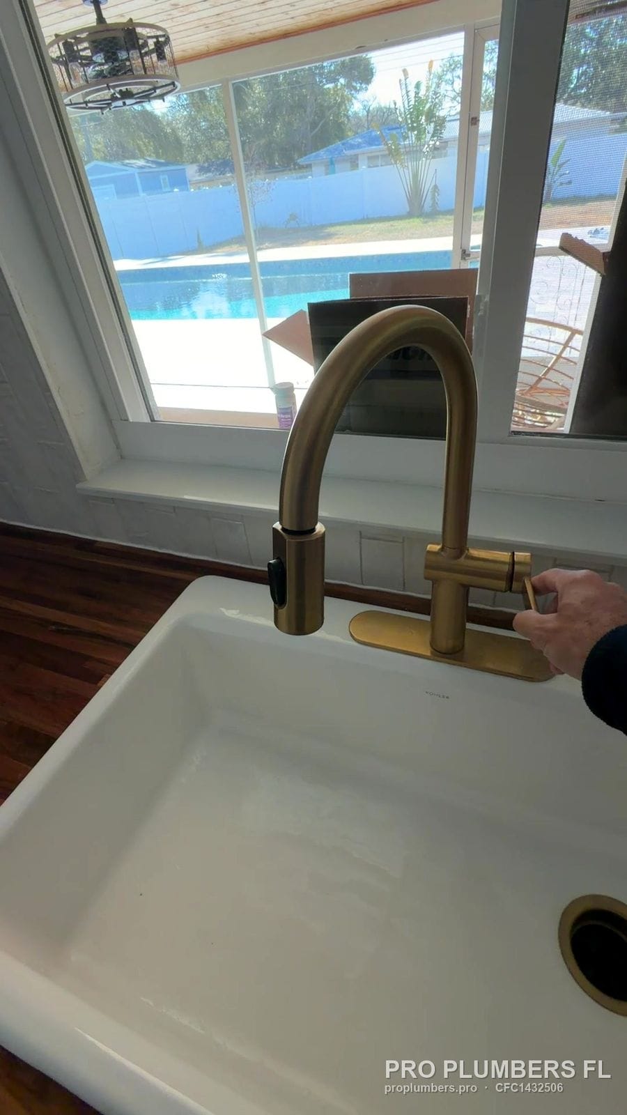 Brushed gold pull-down kitchen faucet on a white farmhouse sink in Clearwater, Florida by PRO PLUMBERS FL, LLC (licence CFC1432506)