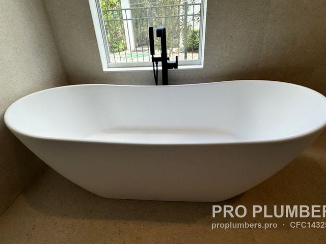 Double-slipper freestanding tub with matte black floor-mounted filler under a window in Westchase, Florida by PRO PLUMBERS FL, LLC (licence CFC1432506)