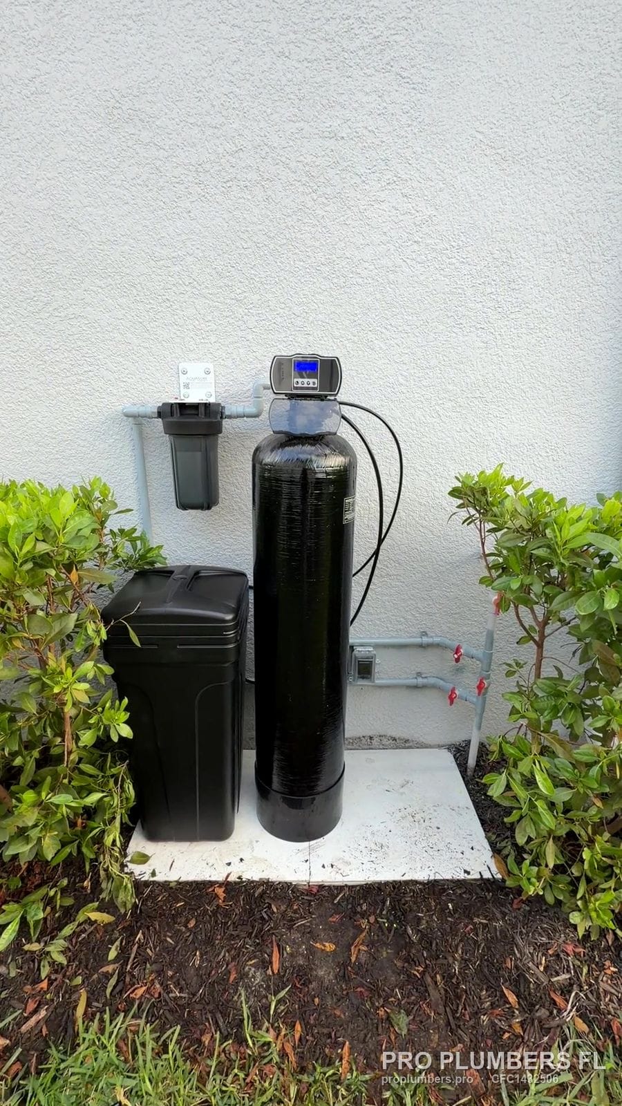 Exterior water softener and brine tank on a concrete pad between shrubs in Sarasota, Florida by PRO PLUMBERS FL, LLC (licence CFC1432506)
