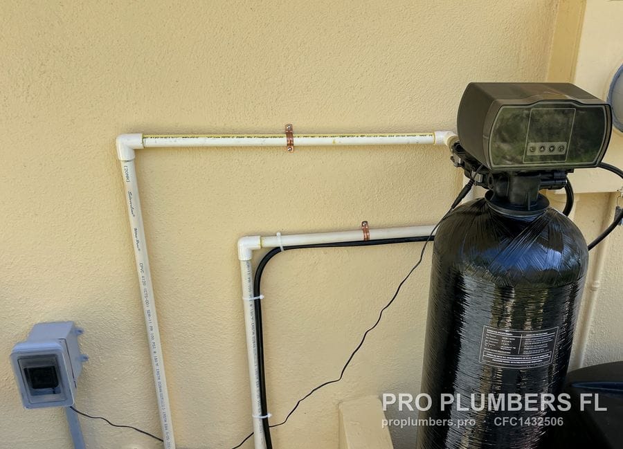 Water softener with digital control head mounted on an exterior stucco wall with a PVC supply loop in Redington Shores, Florida by PRO PLUMBERS FL, LLC (licence CFC1432506)