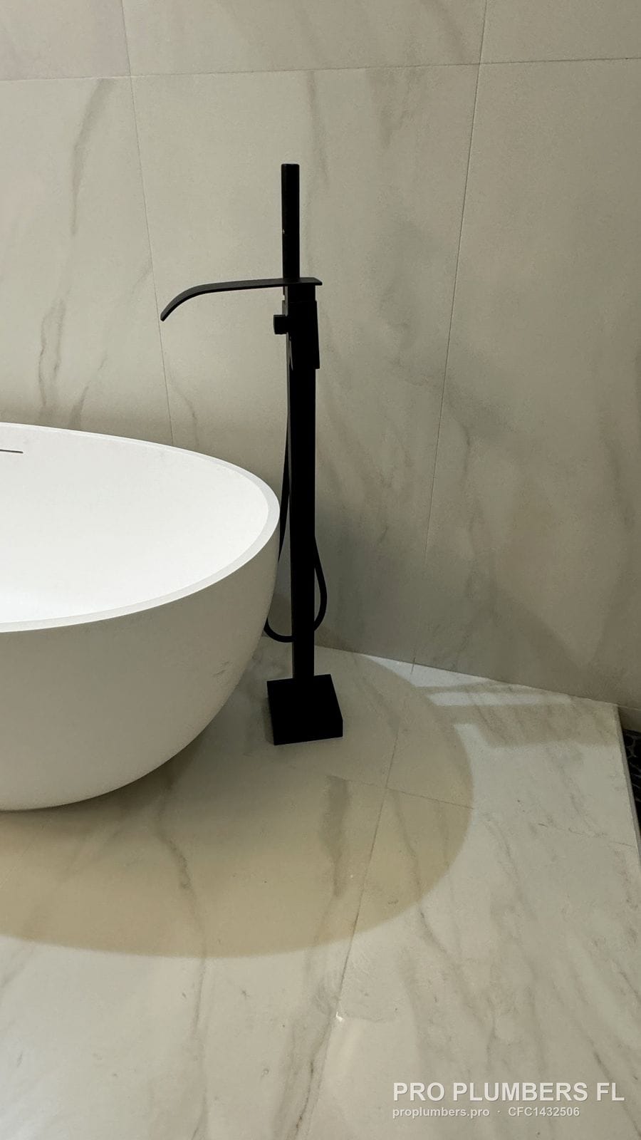 Matte black floor-mounted tub filler with hand shower set beside a freestanding tub in Venice, Florida by PRO PLUMBERS FL, LLC (licence CFC1432506)