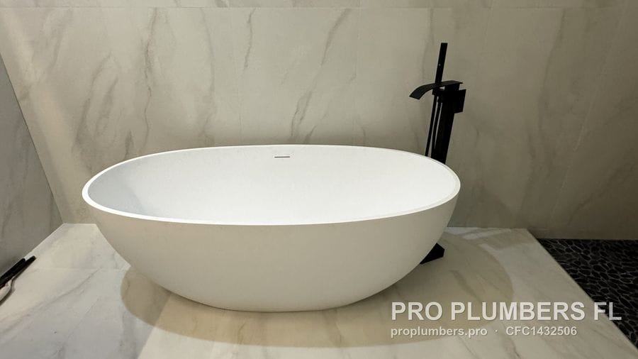 Oval freestanding soaking tub with a matte black floor-mounted tub filler on large-format marble-look tile in Venice, Florida by PRO PLUMBERS FL, LLC (licence CFC1432506)