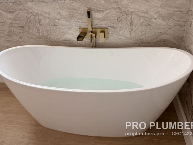 Freestanding slipper tub filled with water under a brushed gold wall-mounted tub filler in Clearwater, Florida by PRO PLUMBERS FL, LLC (licence CFC1432506)