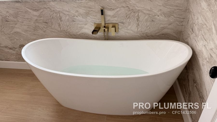 Freestanding slipper tub filled with water under a brushed gold wall-mounted tub filler in Clearwater, Florida by PRO PLUMBERS FL, LLC (licence CFC1432506)