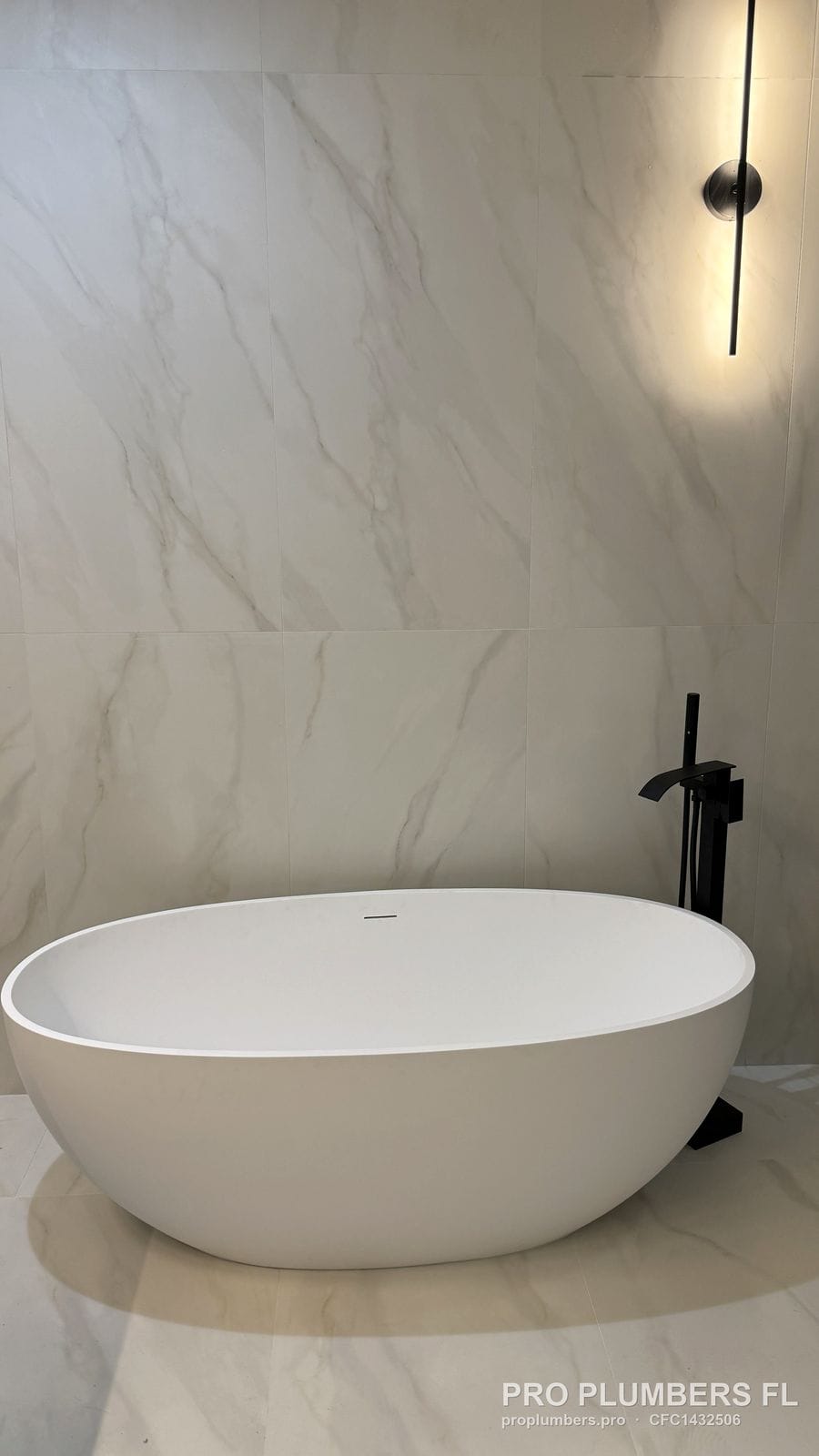 Freestanding soaking tub with floor-mounted filler under a linear wall sconce in Venice, Florida by PRO PLUMBERS FL, LLC (licence CFC1432506)