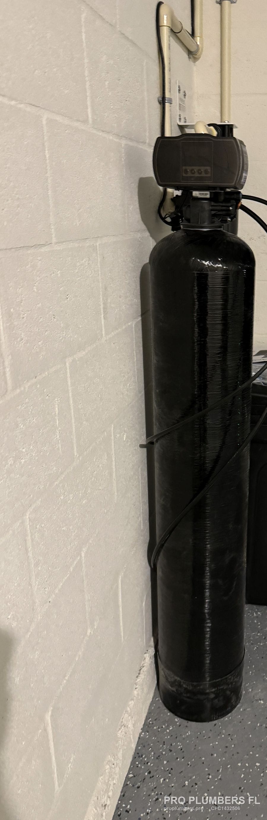 Low-angle view of a garage water softener tank beside the open garage door in Wesley Chapel, Florida by PRO PLUMBERS FL, LLC (licence CFC1432506)
