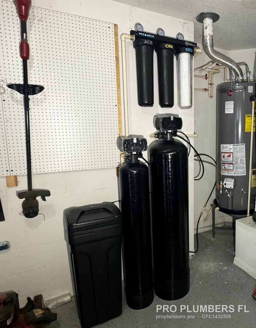 Garage utility wall with softener and carbon tanks, brine tank, three-stage filter rack and water heater in Tampa, Florida by PRO PLUMBERS FL, LLC (licence CFC1432506)