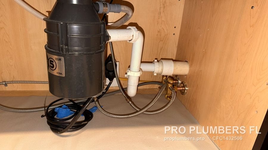 Garbage disposal with a "5" model badge, PVC trap and brass valves under a sink in Tarpon Springs, Florida by PRO PLUMBERS FL, LLC (licence CFC1432506)
