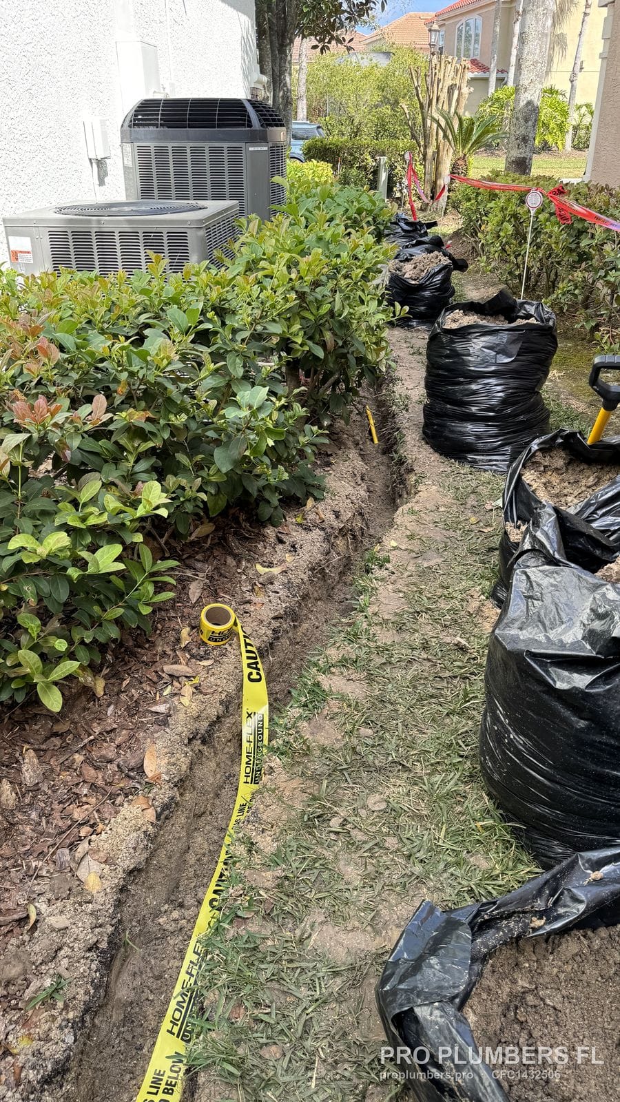Gas line trench along a side yard with caution tape and excavated soil bagged in Westchase, Florida by PRO PLUMBERS FL, LLC (licence CFC1432506)