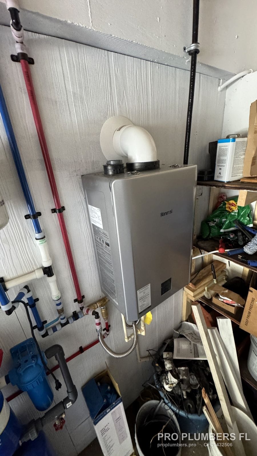 Gas tankless water heater with PVC vent elbow and red and blue PEX lines in Englewood, Florida by PRO PLUMBERS FL, LLC (licence CFC1432506)