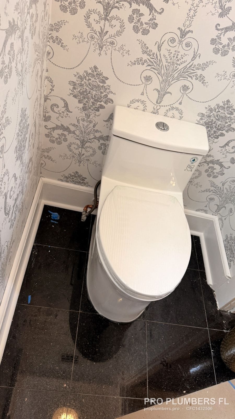 One-piece dual-flush toilet in a powder room with damask wallpaper and black tile floor in Belleair, Florida by PRO PLUMBERS FL, LLC (licence CFC1432506)