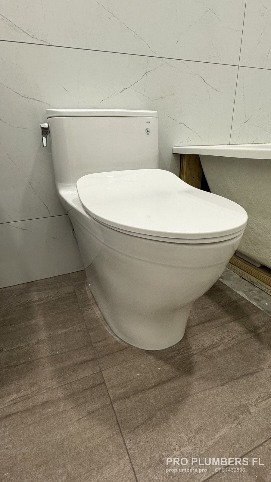 One-piece elongated toilet with soft-close seat installed on large-format floor tile next to a new tub in Westchase, Florida by PRO PLUMBERS FL, LLC (licence CFC1432506)