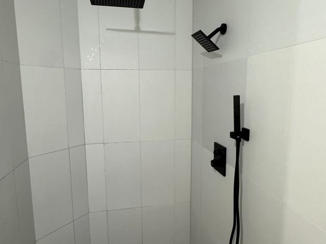 Matte black ceiling rain head, wall shower and handheld in a curbless shower in Dunedin, Florida by PRO PLUMBERS FL, LLC (licence CFC1432506)