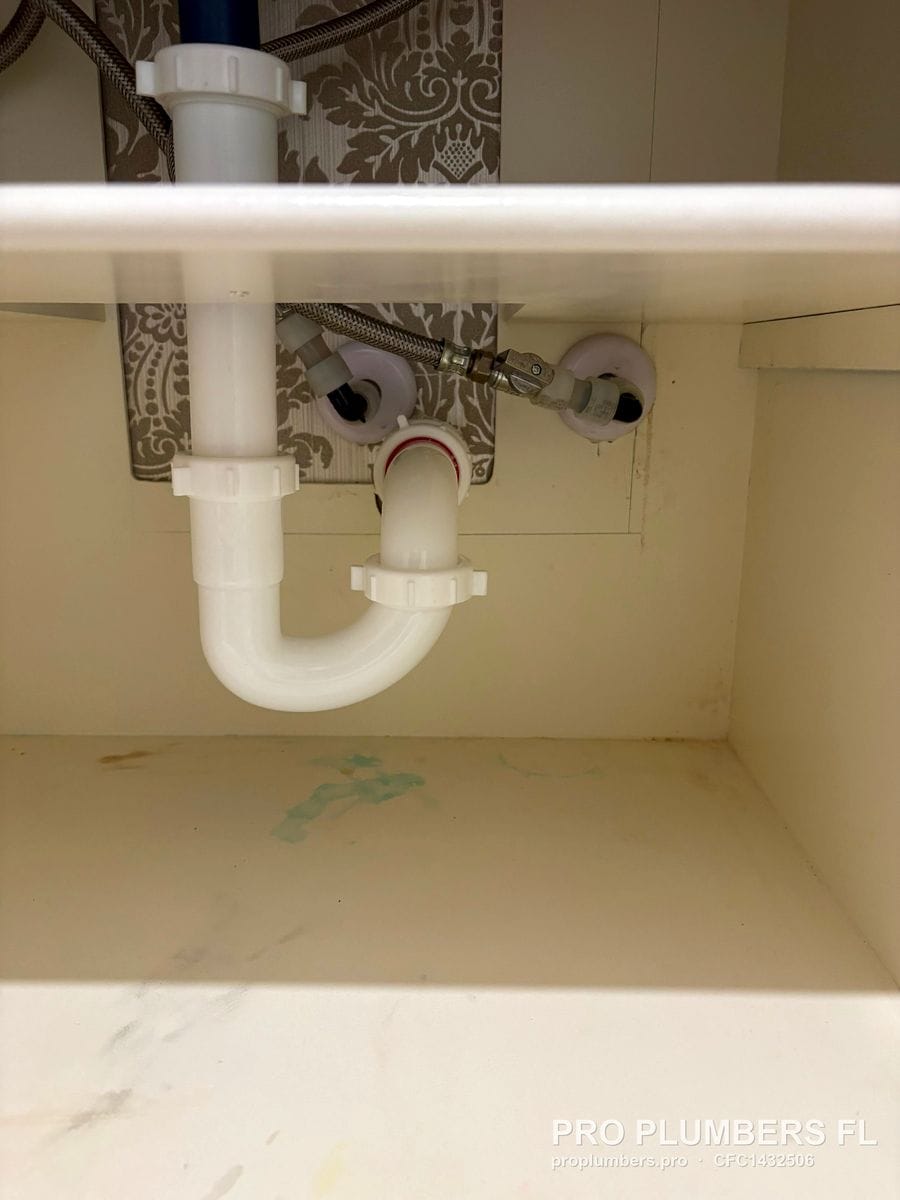 White PVC P-trap and tailpiece inside a vanity cabinet with braided supplies in Clearwater, Florida by PRO PLUMBERS FL, LLC (licence CFC1432506)