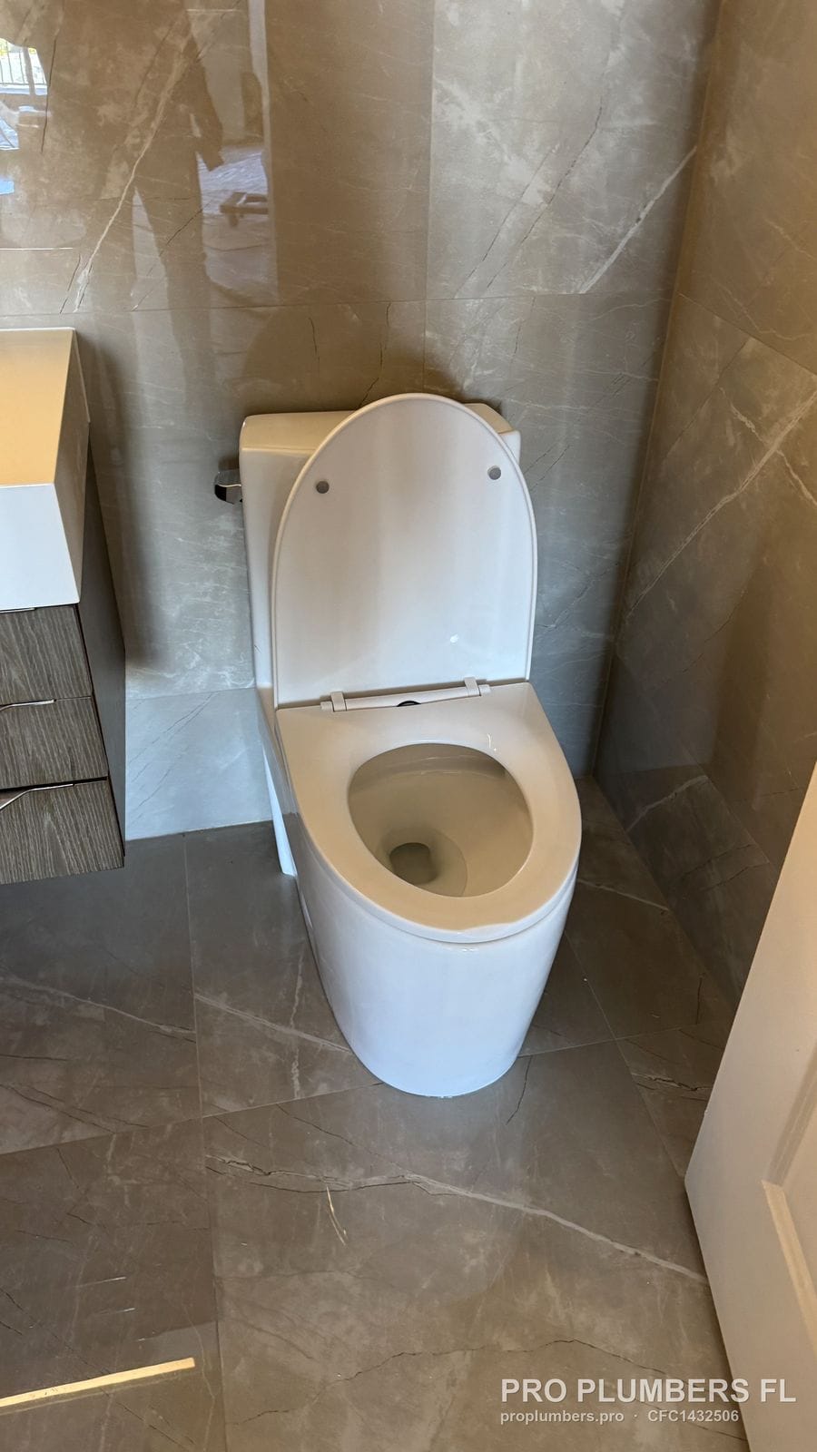 Skirted one-piece toilet with seat open on marble-look porcelain tile beside a floating vanity in Tampa, Florida by PRO PLUMBERS FL, LLC (licence CFC1432506)