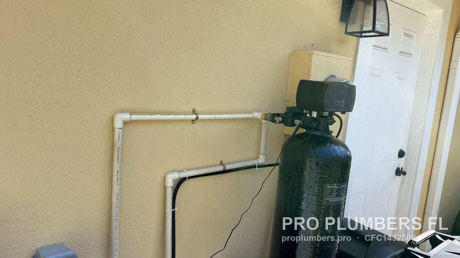 PVC supply and return loop routed across an exterior wall into a water softener control head in Redington Shores, Florida by PRO PLUMBERS FL, LLC (licence CFC1432506)