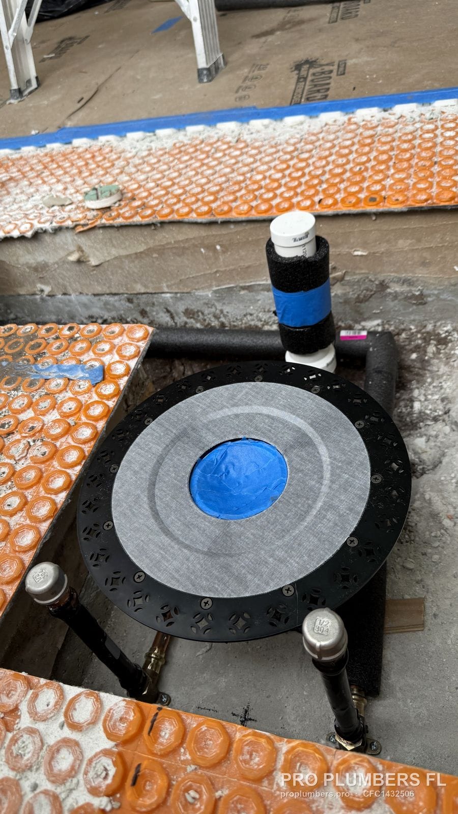 Round rough-in plate with test cap and PVC drain riser before tile, orange membrane around the opening in East Lake, Florida by PRO PLUMBERS FL, LLC (licence CFC1432506)