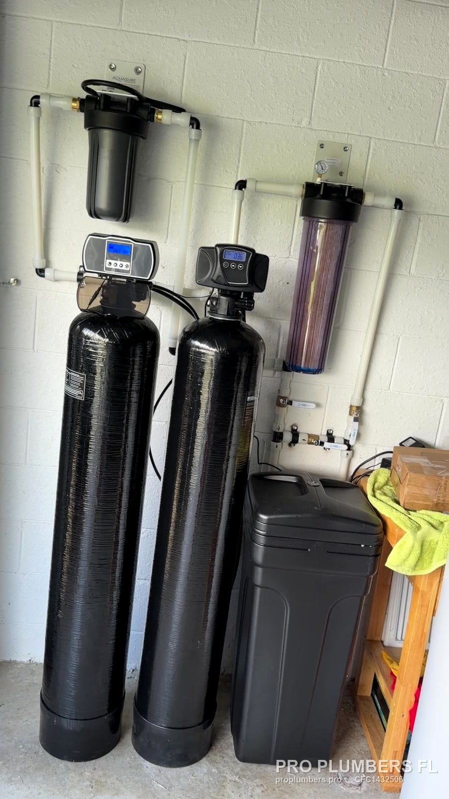 Twin water treatment tanks with digital control heads, brine tank and prefilters on a block wall in Bradenton, Florida by PRO PLUMBERS FL, LLC (licence CFC1432506)