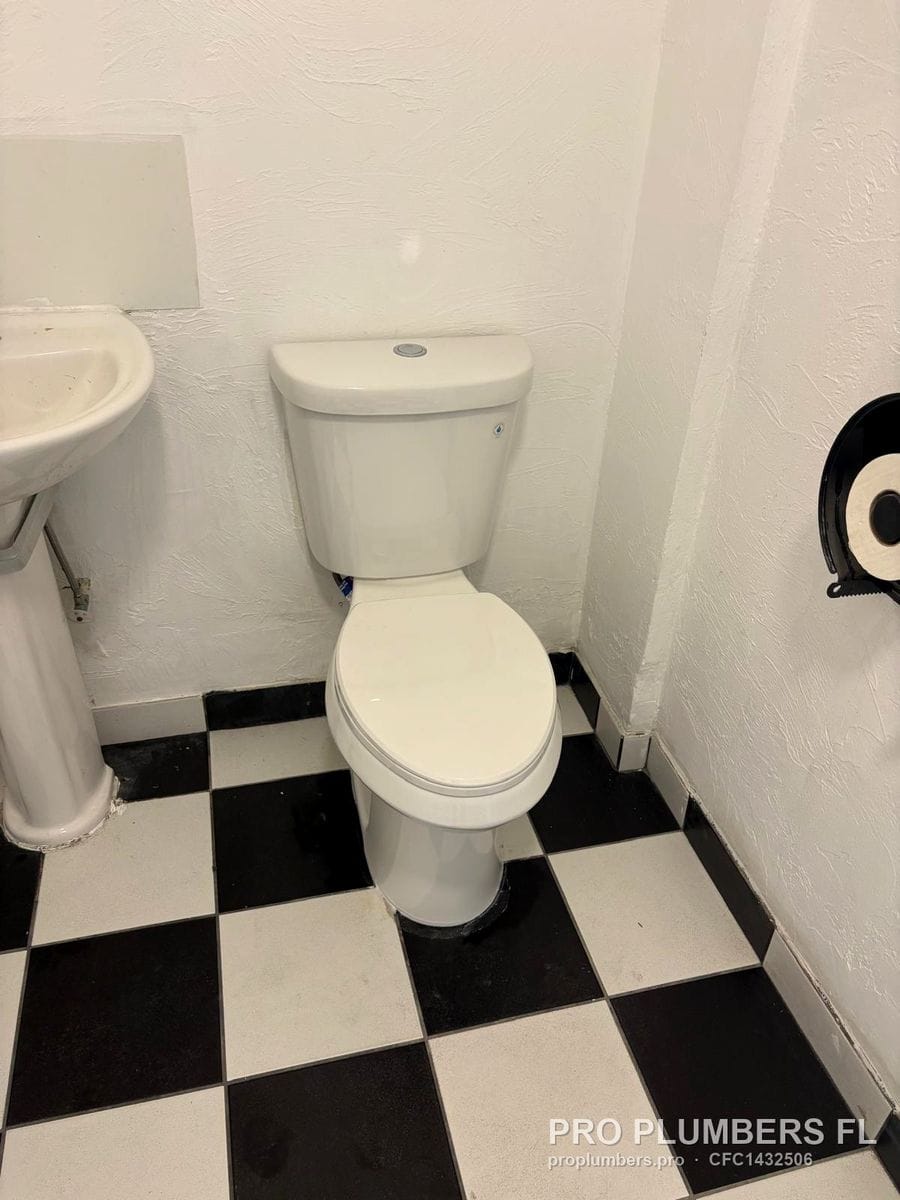 Two-piece toilet on black and white checkerboard floor next to a pedestal sink in Clearwater, Florida by PRO PLUMBERS FL, LLC (licence CFC1432506)