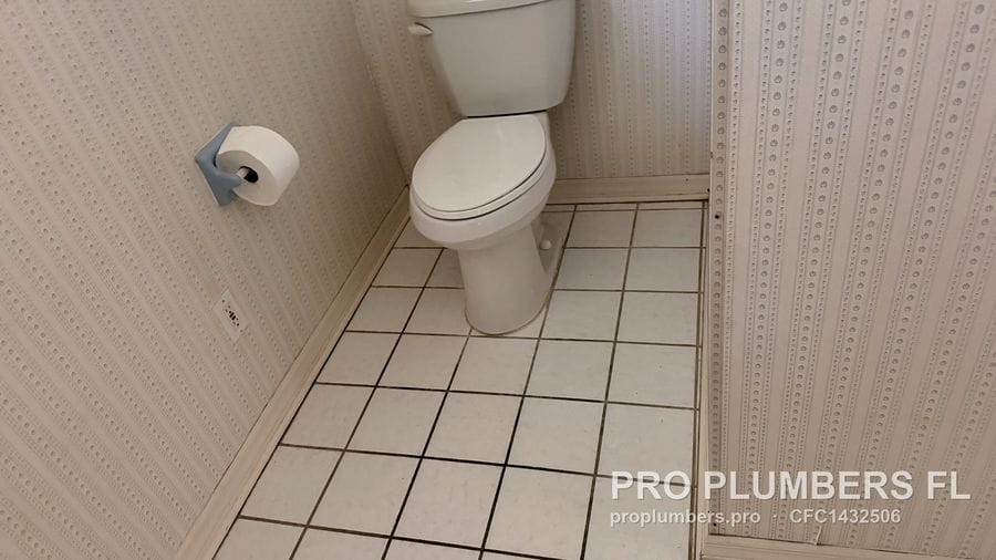 Two-piece toilet installed in a small bathroom with white floor tile and textured wall panels in Clearwater, Florida by PRO PLUMBERS FL, LLC (licence CFC1432506)