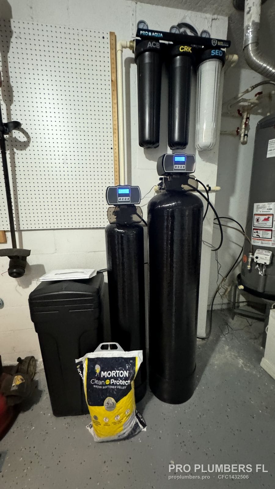 Softener and carbon tanks with lit digital heads under a three-stage PRO AQUA filter rack in Tampa, Florida by PRO PLUMBERS FL, LLC (licence CFC1432506)