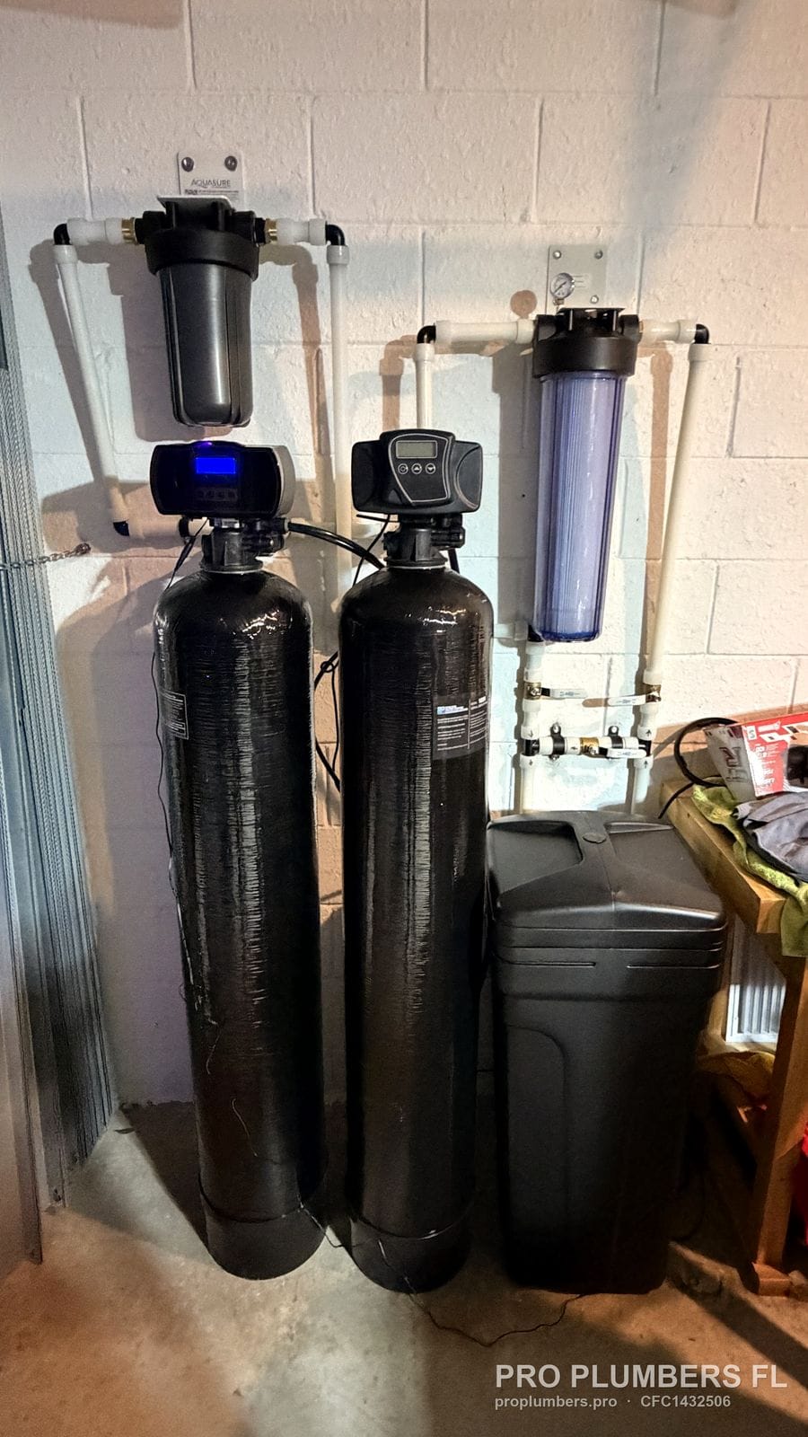 Two tanks with digital heads, brine tank, black sediment housing and clear filter housing on a garage wall in Bradenton, Florida by PRO PLUMBERS FL, LLC (licence CFC1432506)